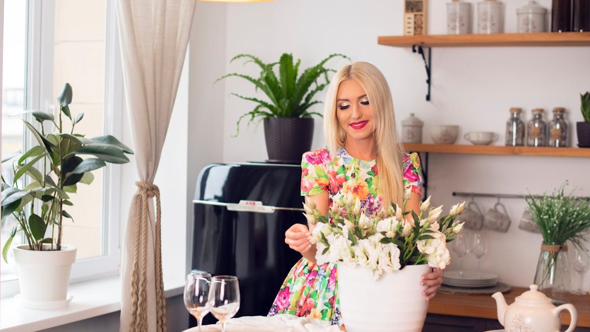 A woman arranges flowers in a stylish, modern kitchen with natural light.